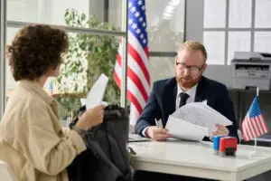 Portrait of male worker revising documents of young woman applying for visa in us immigration office